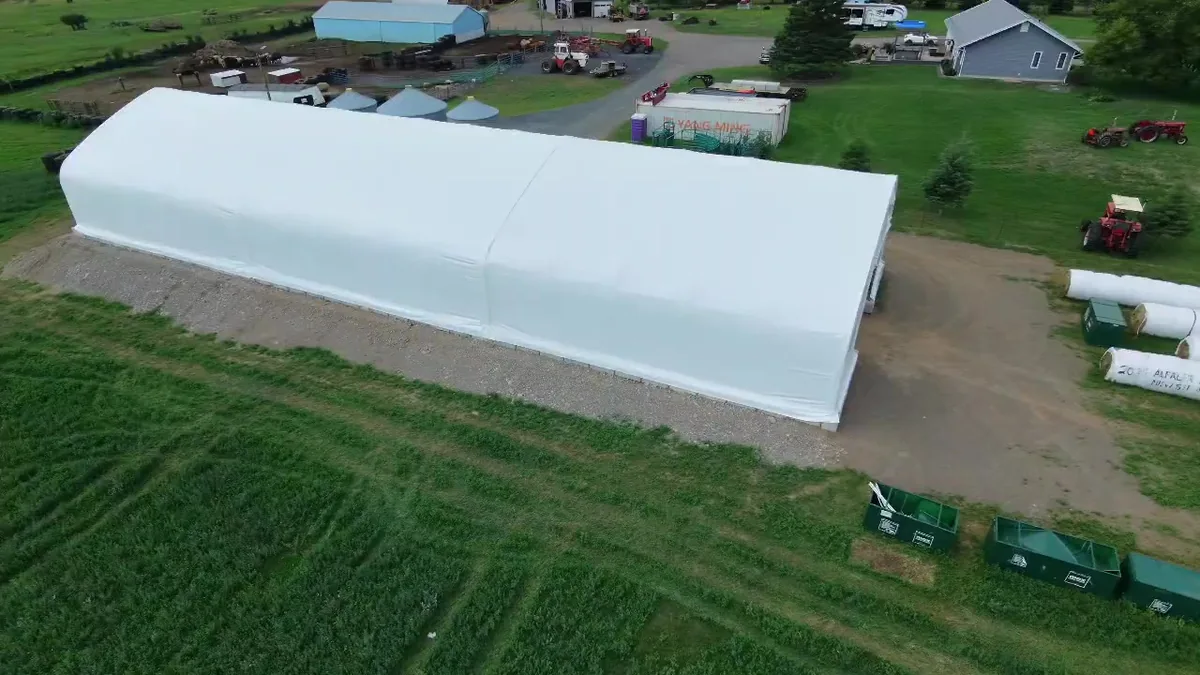 Aerial side view of the white covered building and surrounding farm