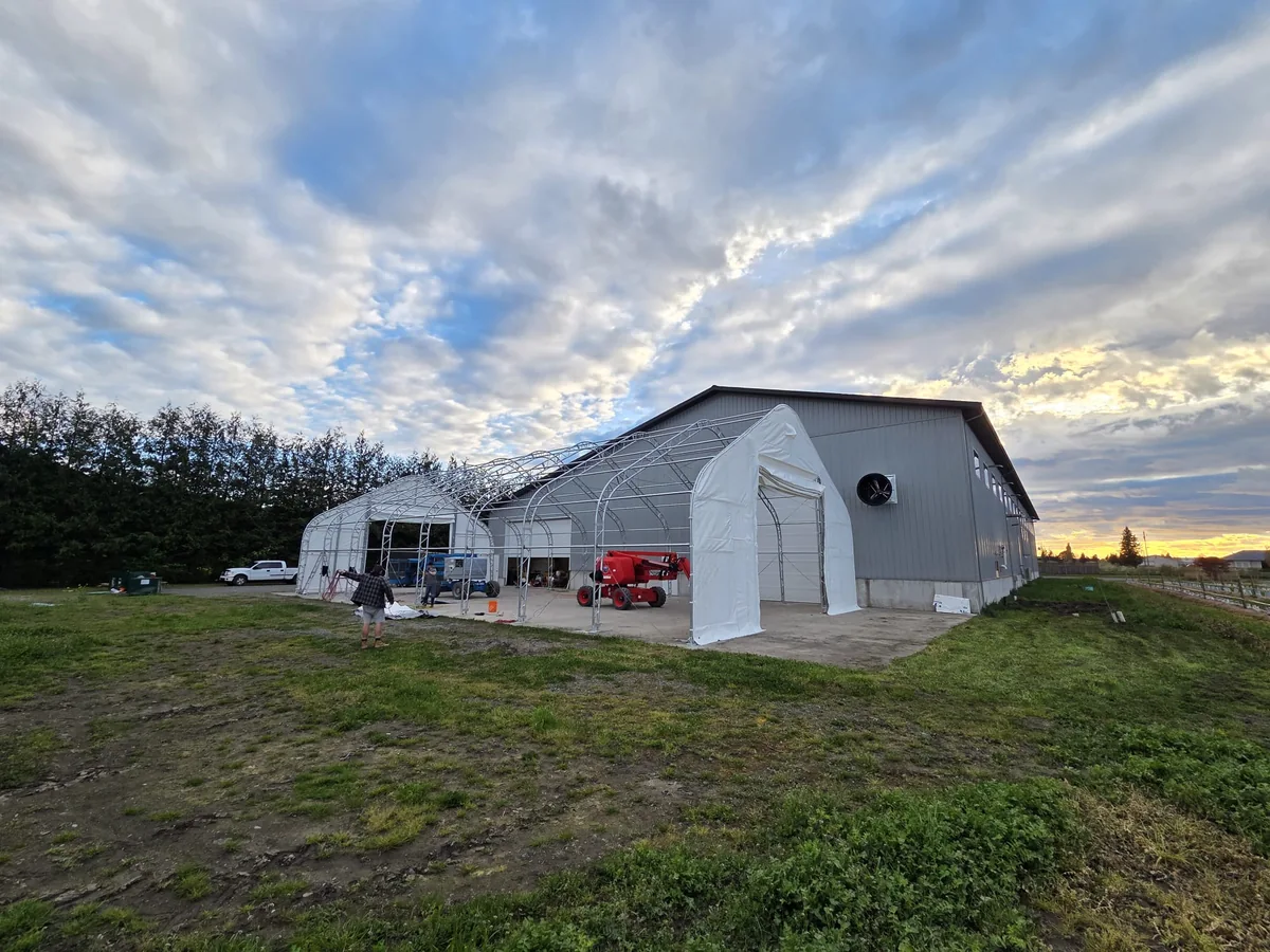 Fabric endwalls and open roof framing beside a metal building at sunset