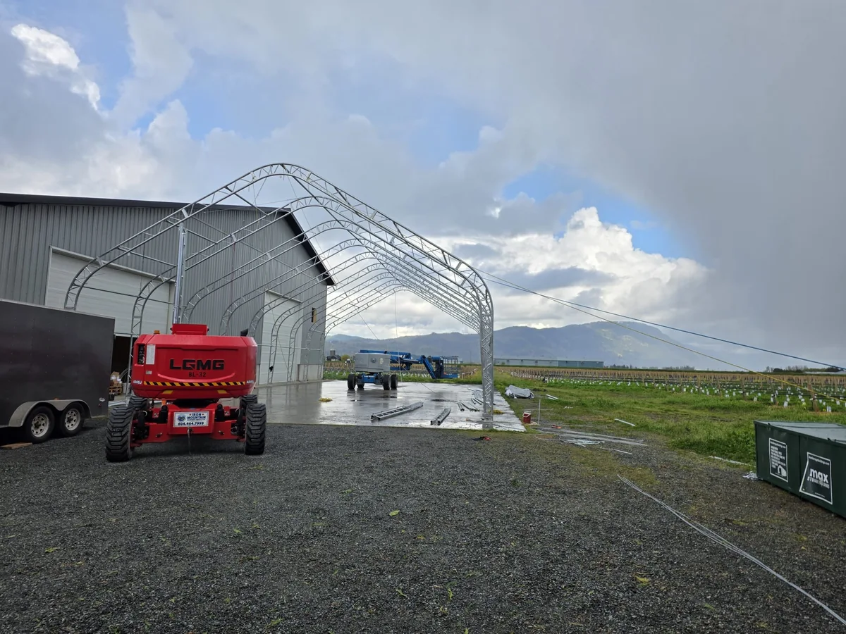Steel arches and two boom lifts beside an existing metal building
