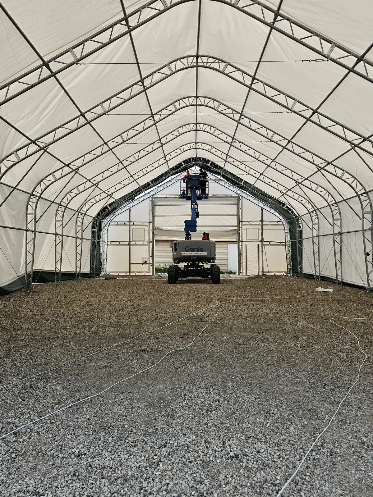 Crew on a blue boom lift inside a covered fabric building